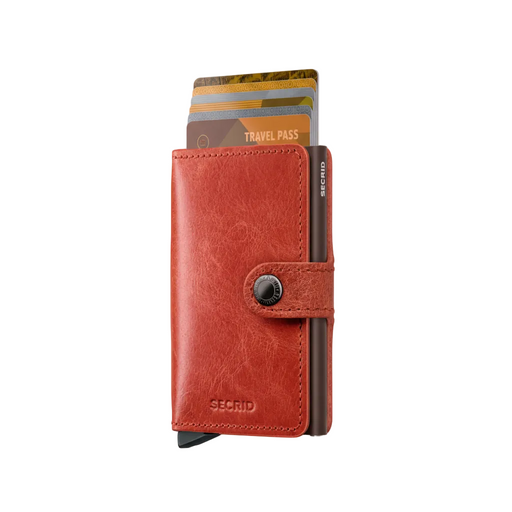 A red leather Secrid Miniwallet with a snap-button closure, shown standing upright with several cards partially inserted. The Secrid brand name is visible on the lower left and vertically on the card edge.