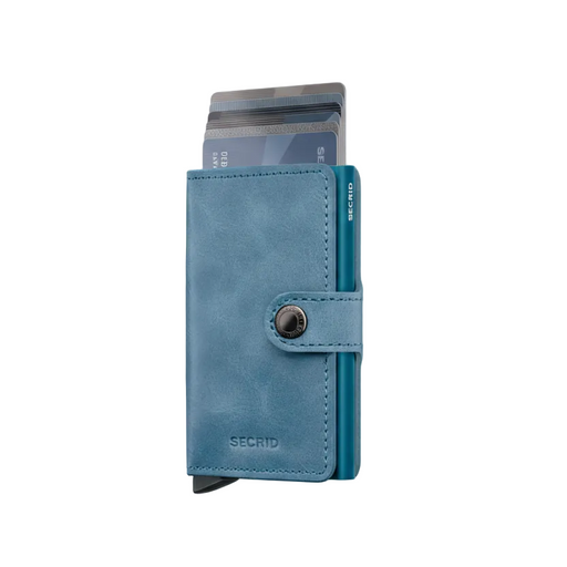 A blue Secrid minimalist cardholder wallet with a snap button closure, shown with several cards partially inserted, on a clean white background.