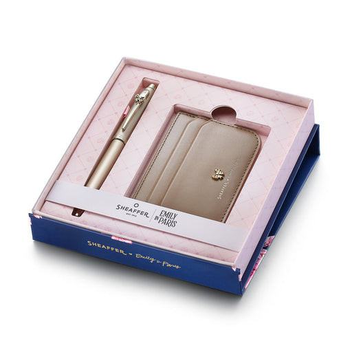 Sheaffer 100 Emily in Paris gift set featuring a champagne gold ballpoint pen with a gold-shaped clip emblem and full-grain credit card holder in a premium presentation box. Model G2937751-2