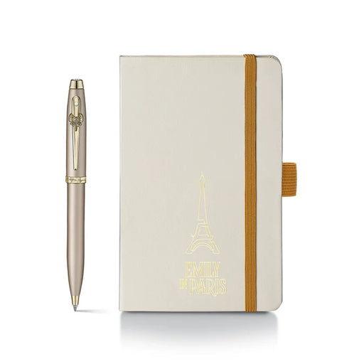 Sheaffer 100 Emily in Paris gift set featuring a champagne gold ballpoint pen with a bow-shaped clip emblem and a matching hardbound small notebook. Model G2937751-4