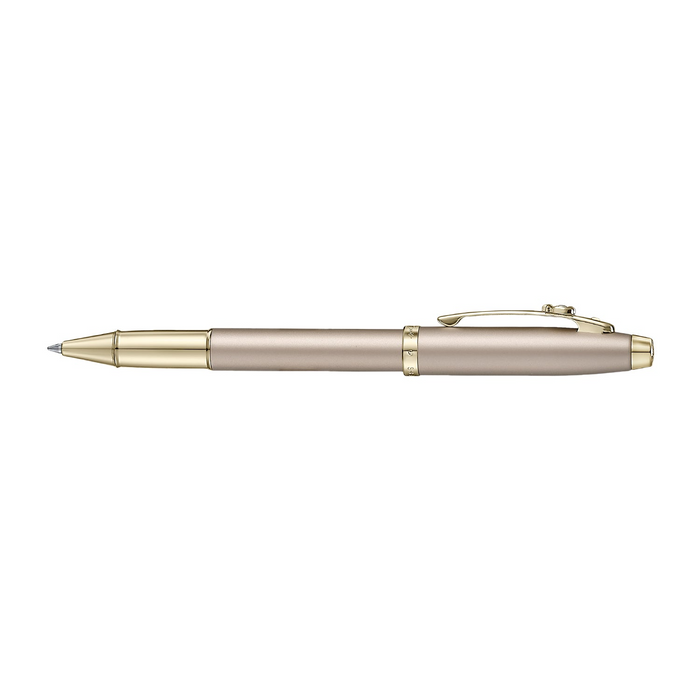 A sleek Sheaffer 100  Emily in Paris rollerball pen in a metallic champagne gold lacquer finish with champagne gold  trims and adorned with a bow-shaped emblem on the clip. Model E1937751