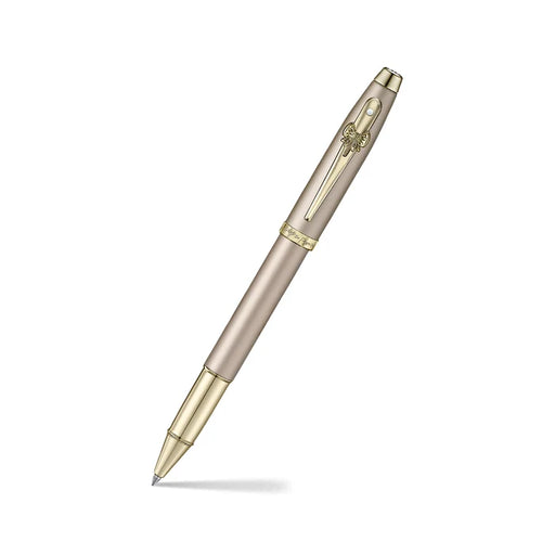 A sleek Sheaffer 100  Emily in Paris rollerball pen in a metallic champagne gold lacquer finish with champagne gold  trims and adorned with a bow-shaped emblem on the clip. Model E1937751