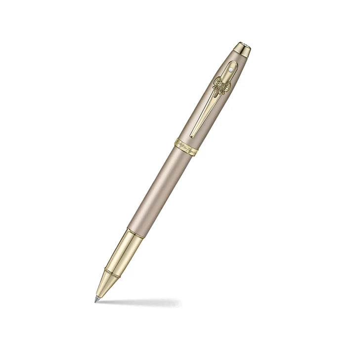 A sleek Sheaffer 100  Emily in Paris rollerball pen in a metallic champagne gold lacquer finish with champagne gold  trims and adorned with a bow-shaped emblem on the clip. Model E1937751