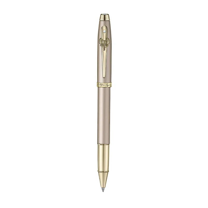 A sleek Sheaffer 100  Emily in Paris rollerball pen in a metallic champagne gold lacquer finish with champagne gold  trims and adorned with a bow-shaped emblem on the clip. Model E1937751