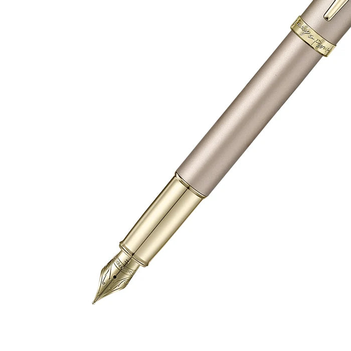The forepart of a sleek Sheaffer 100  Emily in Paris fountain pen in a metallic champagne gold lacquer finish with champagne gold  trims and adorned with a bow-shaped emblem on the clip . Model E0937753