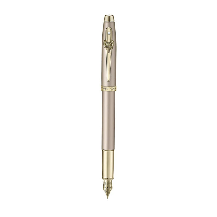 A sleek Sheaffer 100  Emily in Paris fountain pen in a metallic champagne gold lacquer finish with champagne gold  trims and adorned with a bow-shaped emblem on the clip . Model E0937753
